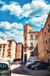 Calle urbana con torre de ladrillo y edificios históricos en Toledo.