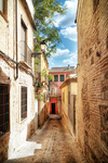 Callejón de piedra con vegetación y luz al fondo en Toledo.