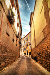 Callejón empedrado entre muros de ladrillo y piedra en Toledo.