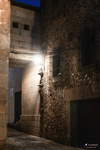 Rincón nocturno con muro de piedra y farol en una calle antigua de Cáceres.