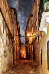 Callejuela empedrada con luz cálida nocturna en el casco antiguo de Cáceres.