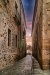 Callejón estrecho de piedra bajo cielo de atardecer en Cáceres.