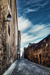 Calle empedrada entre muros históricos bajo cielo azul en Cáceres.