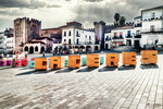 Plaza Mayor de Cáceres con torre al fondo y elementos de color en primer plano.