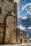 Iglesia de piedra con torre y cielo nublado en Cáceres.