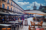 Plaza con terrazas y edificios históricos bajo cielo nublado en León.
