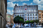 Plaza urbana con edificio histórico y árboles podados en León.