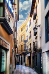 Calle estrecha con fachadas altas y luz lateral en León.