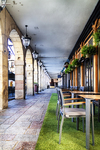Galería porticada con sillas verdes y columnas en León.