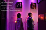 Sala de exposición iluminada en tonos violetas con visitantes observando obras.