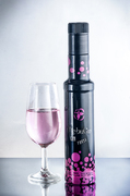 Bodegón de botella negra con copa de bebida rosada sobre fondo claro.