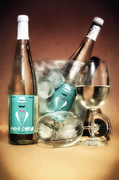 Bodegón de botellas de bebida, cubitera y copas sobre fondo cálido.