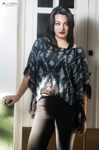Eva posa de pie junto a una puerta blanca, con blusa azul estampada y pantalón negro.