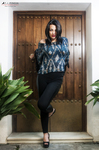 Eva de pie ante una puerta de madera, con blusa estampada, pantalón negro y tacones.