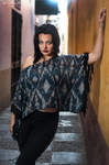 Eva posa de pie en una escalera, con blusa amplia azul estampada y pantalón negro.