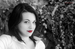 Retrato en blanco y negro de Eva con labios rojos, sobre fondo vegetal desenfocado.