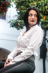 Eva sentada al aire libre con camisa blanca, pantalón gris y mirada hacia un lado.