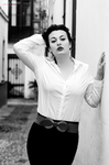 Eva posa en blanco y negro con camisa blanca, apoyada junto a una pared.
