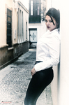 Eva posa de perfil en una calle estrecha, con camisa blanca y pantalón negro.