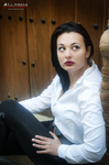 Eva sentada ante una puerta de madera, con camisa blanca y pantalón negro.