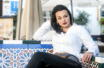 Eva recostada en un banco de azulejos, con camisa blanca y pose relajada.