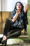 Eva sentada en un interior claro, con blusa azul estampada y gesto sensual.