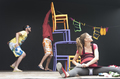 Escena teatral de Caravan con actores y sillas de colores en movimiento.