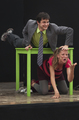 Actor con traje gris interactúa con una actriz en una escena teatral de Caravan.
