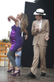 Personajes teatrales vestidos de morado y beige actúan juntos sobre el escenario.