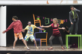 Representación teatral de Caravan sobre escenario móvil con actores y sillas de colores.