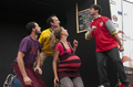 Grupo de actores en movimiento interpreta una escena teatral con vestuario colorido.