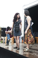 Dos mujeres permanecen junto al escenario móvil durante una actividad teatral al aire libre.