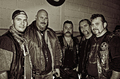 Grupo de hombres con ropa motera posa en una escena de estética rockera y urbana.