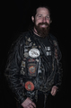 Retrato frontal de un hombre barbudo con chaleco motero lleno de parches.