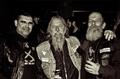 Tres hombres con chalecos moteros posan juntos en una fotografía de tono sepia.