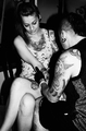 Dos personas sentadas en una escena íntima de bar con estética de tatuajes y noche.