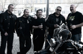 Grupo de hombres reunidos al aire libre junto a motos en una concentración motera.