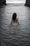 África permanece de espaldas dentro del mar, con el agua a la altura del pecho y la cala al fondo.