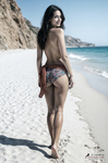 Chloe camina por la arena junto al mar, vista desde atrás en una playa mediterránea.