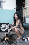 Chloe prepara comida en una pequeña hoguera junto a la caravana aparcada cerca de la playa.